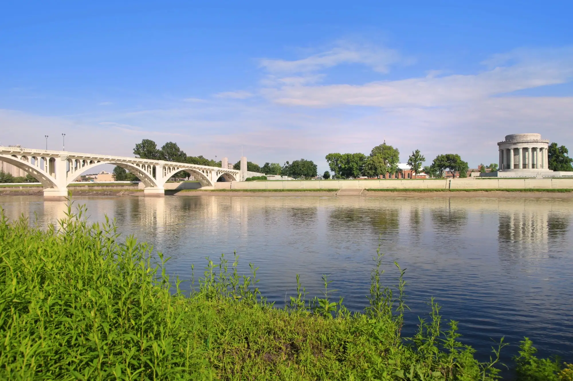  A scenic view of the George Rogers Clark Memorial and the Lincoln Memorial Bridge spanning the Wabash River in Vincennes, Indiana, under a clear blue sky.